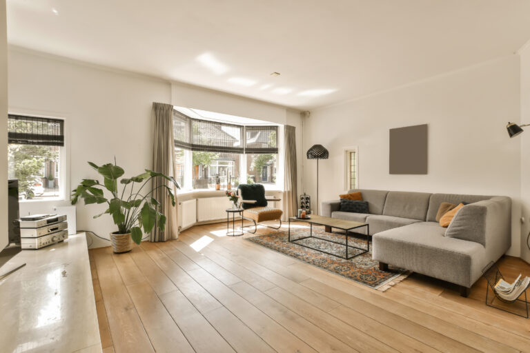 a living room with hardwood flooring and white walls there is a grey couch in front of the gray sofa